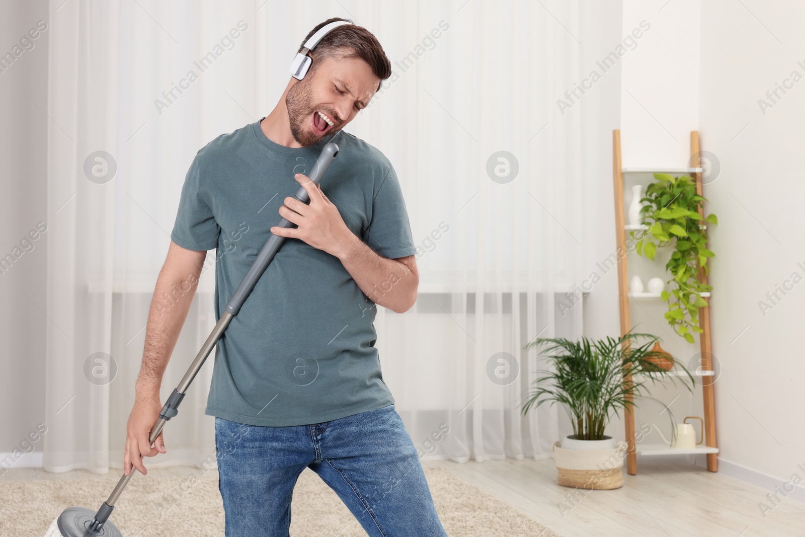 Photo of Enjoying cleaning. Happy man with mop singing while tidying up at home, space for text