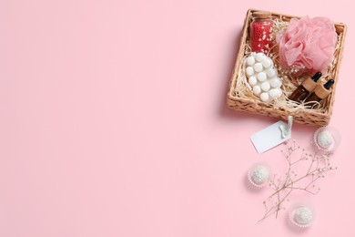 Photo of Spa gift set of different luxury products in wicker basket on pale pink background, flat lay. Space for text