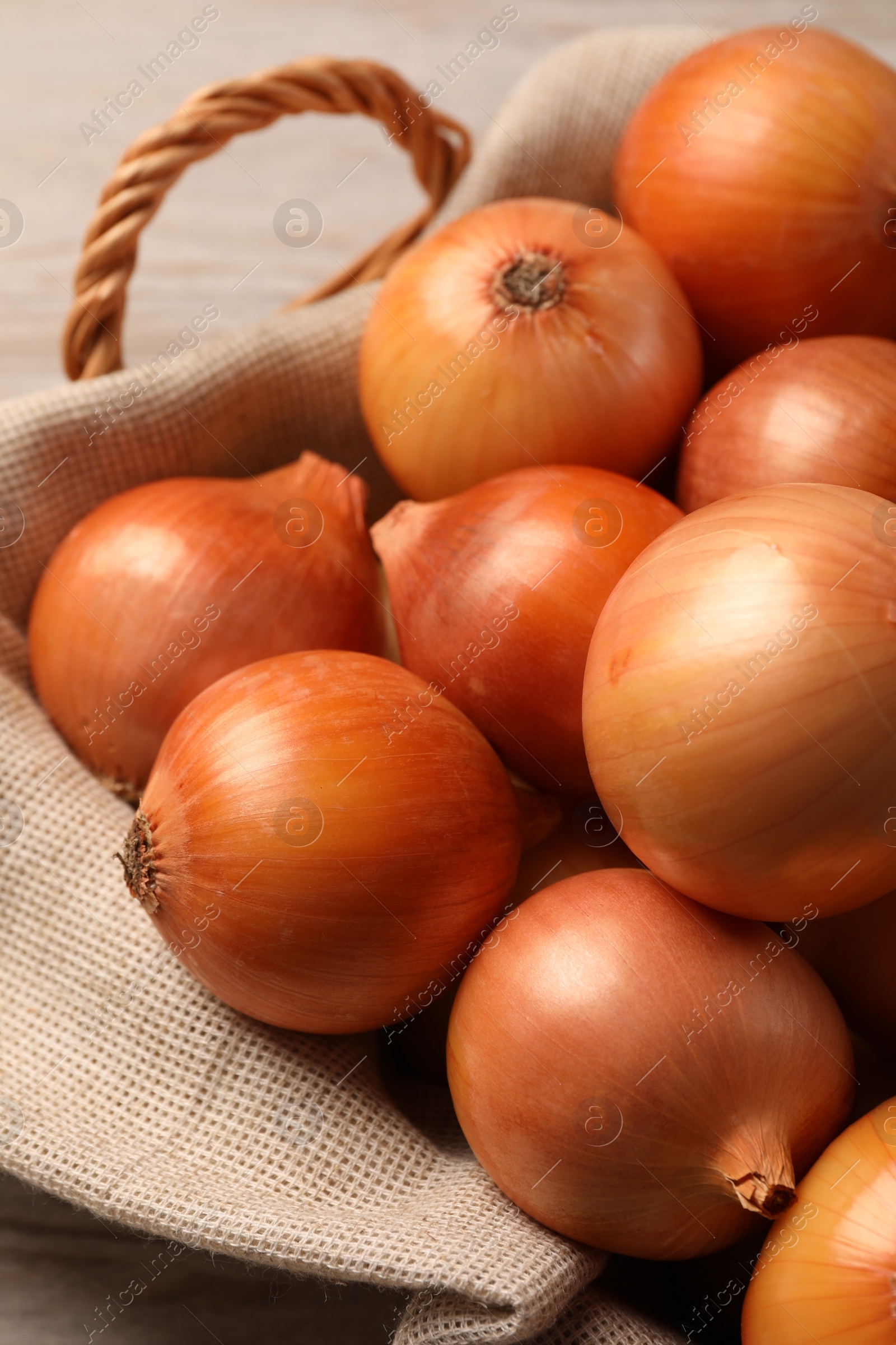 Photo of Wicker basket with many ripe onions on wooden table, closeup