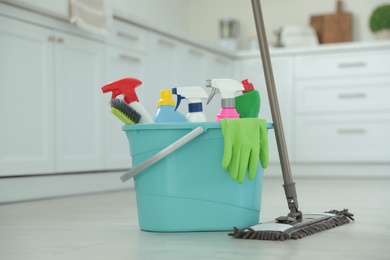 Photo of Mop and plastic bucket with different cleaning supplies in kitchen