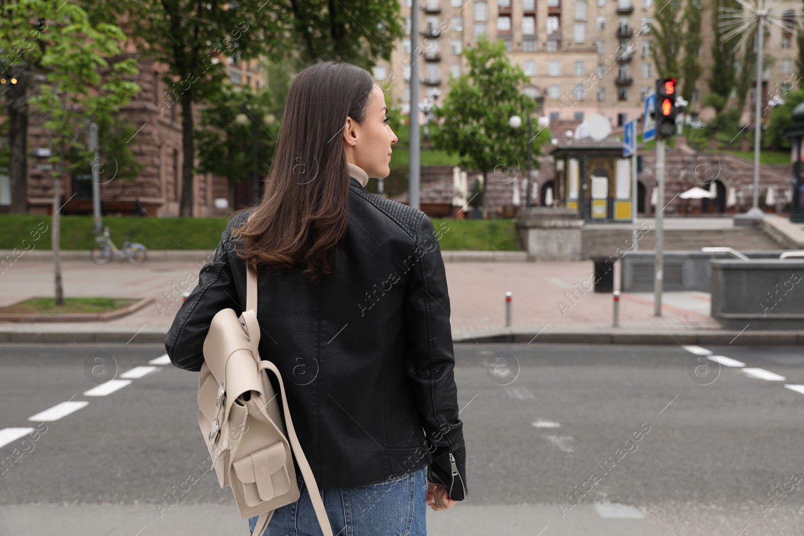 Photo of Young woman waiting at traffic lights to cross street, back view