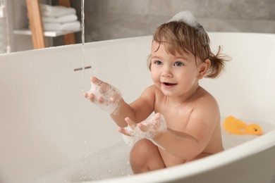 Photo of Cute little girl taking bubble bath indoors. Space for text