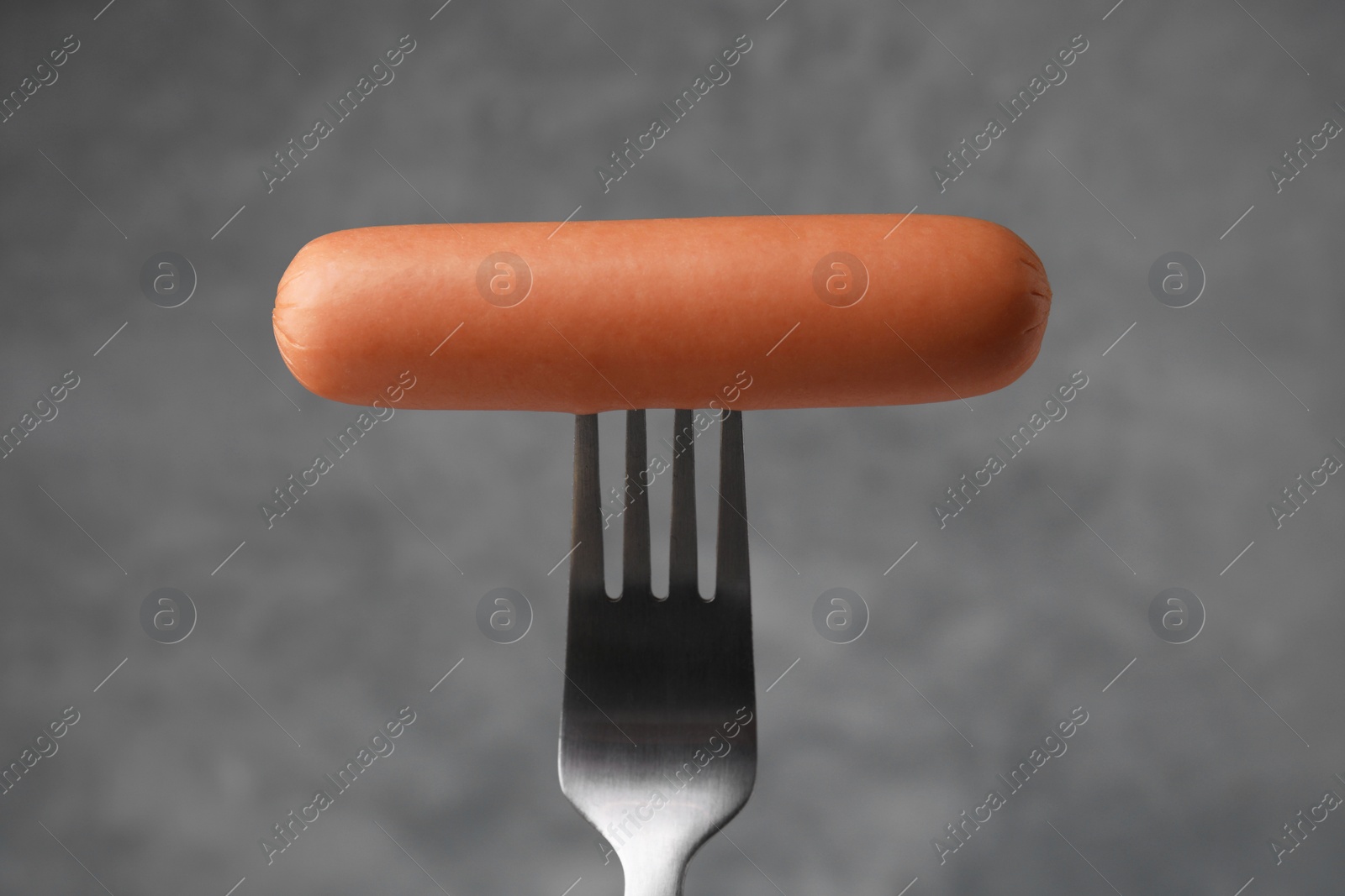 Photo of Delicious boiled sausage on fork against grey background, closeup