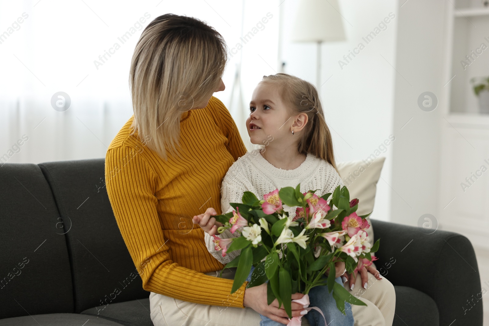 Photo of Little daughter congratulating her mom with Mother`s Day at home. Woman holding bouquet of alstroemeria flowers