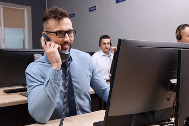 Photo of Handsome call center operator talking on phone and his colleagues working in modern office