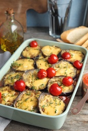 Baked eggplant with tomatoes and cheese in dishware on wooden table