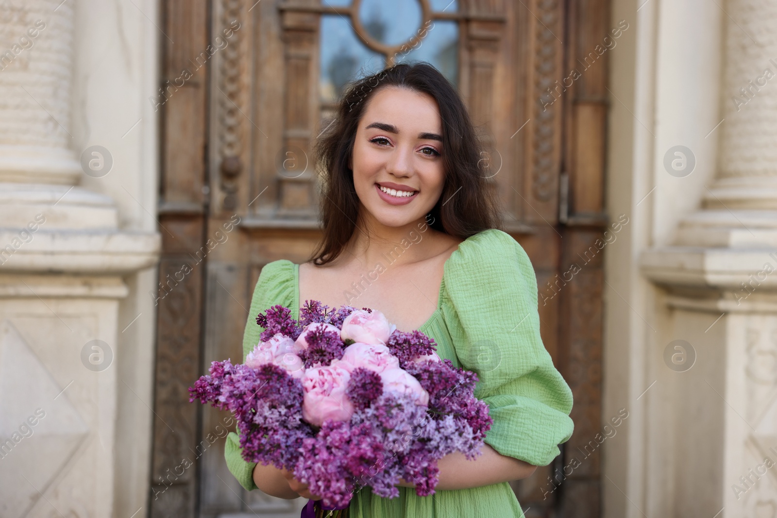 Photo of Beautiful woman with bouquet of spring flowers near building outdoors