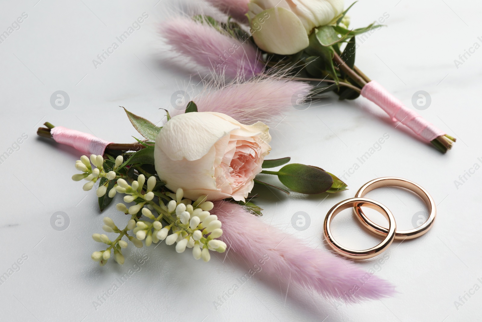 Photo of Small stylish boutonnieres and rings on white marble table