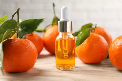 Bottle of tangerine essential oil and fresh fruits on white wooden table, closeup