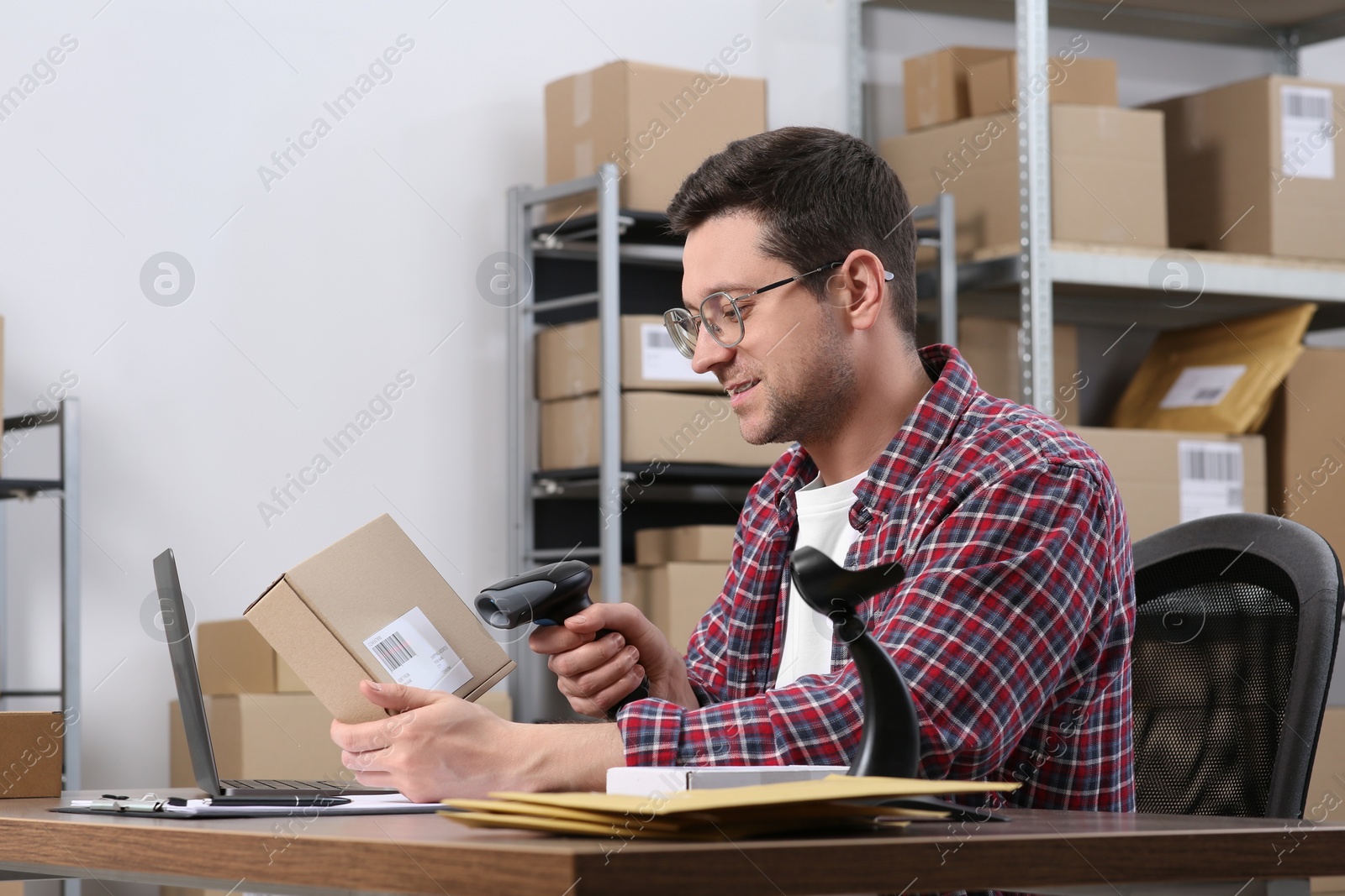 Photo of Seller with scanner reading parcel barcode at table in office. Online store