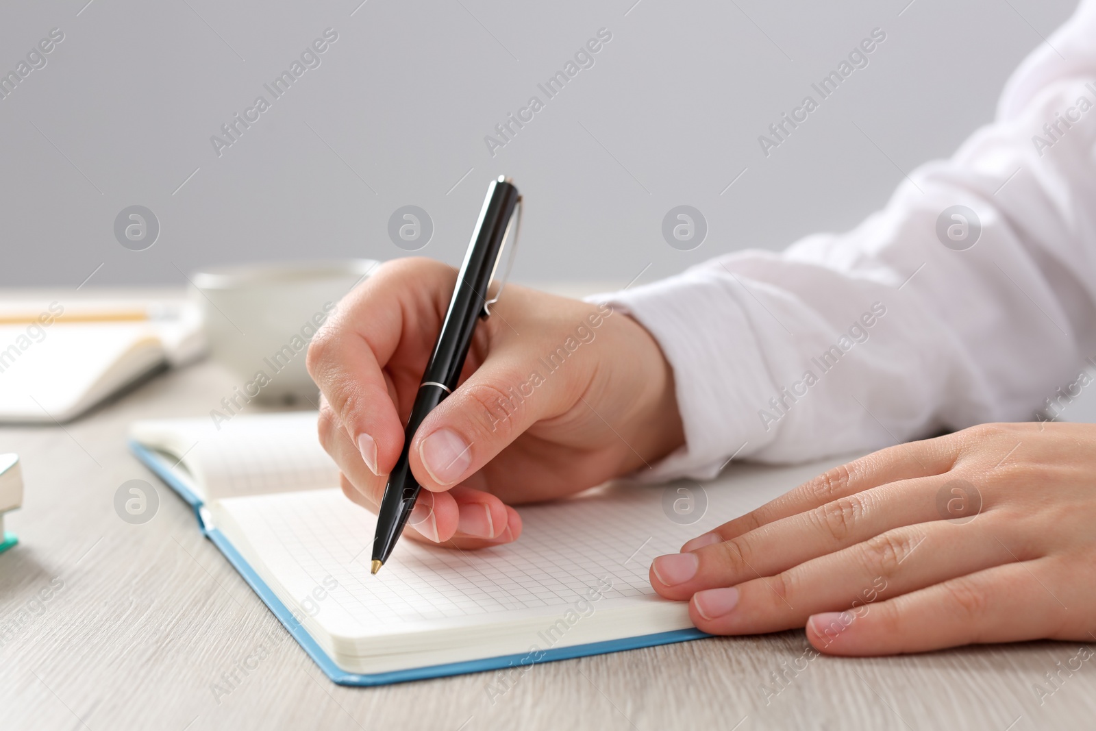 Photo of Woman writing in notebook at wooden table in office, closeup