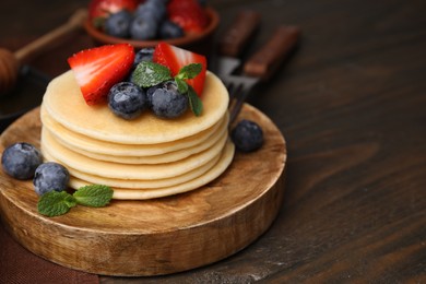 Photo of Delicious pancakes with strawberries, blueberries and mint on wooden table, closeup. Space for text