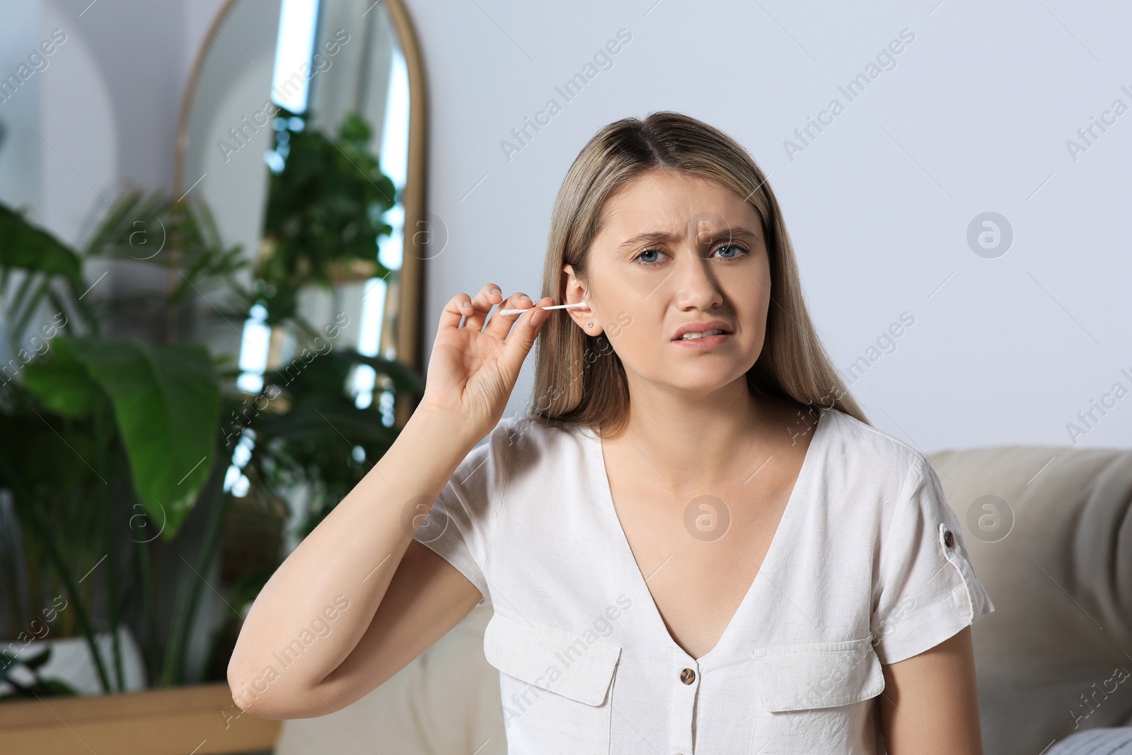 Photo of Young woman cleaning ear with cotton swab at home