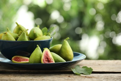 Photo of Cut and whole green figs on wooden table against blurred background, space for text