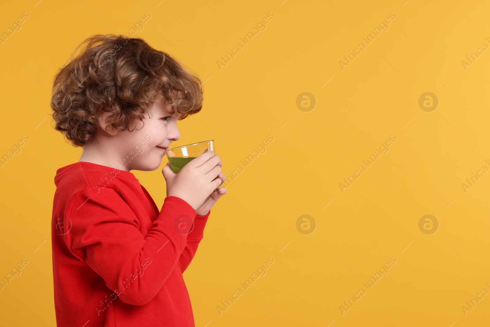 Photo of Cute little boy drinking fresh juice on orange background, space for text