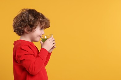 Photo of Cute little boy drinking fresh juice on orange background, space for text