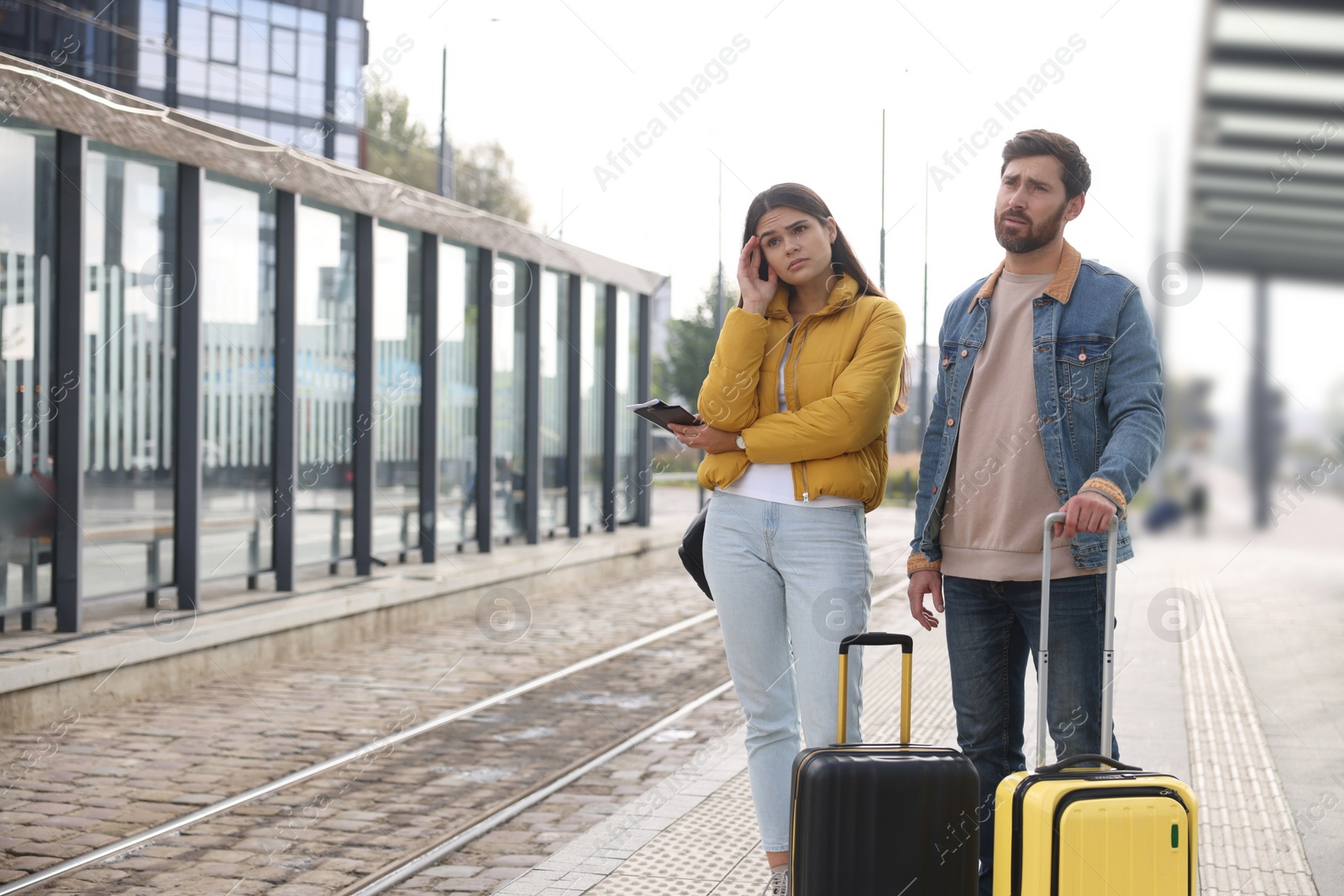 Photo of Being late. Worried couple with suitcases waiting at tram station outdoors, space for text