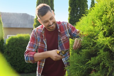 Photo of Happy man cutting bush outdoors on sunny day. Gardening time
