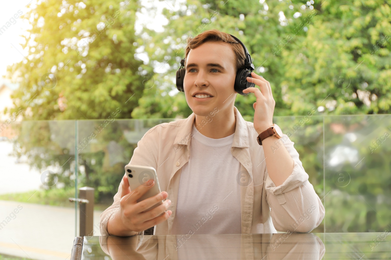 Photo of Handsome young man with headphones and smartphone at table in outdoor cafe