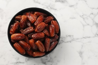 Photo of Sweet dried dates in bowl on white marble table, top view. Space for text