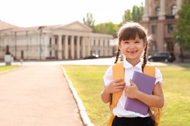 Photo of Little girl with backpack and notebook outdoors. Stationery for school