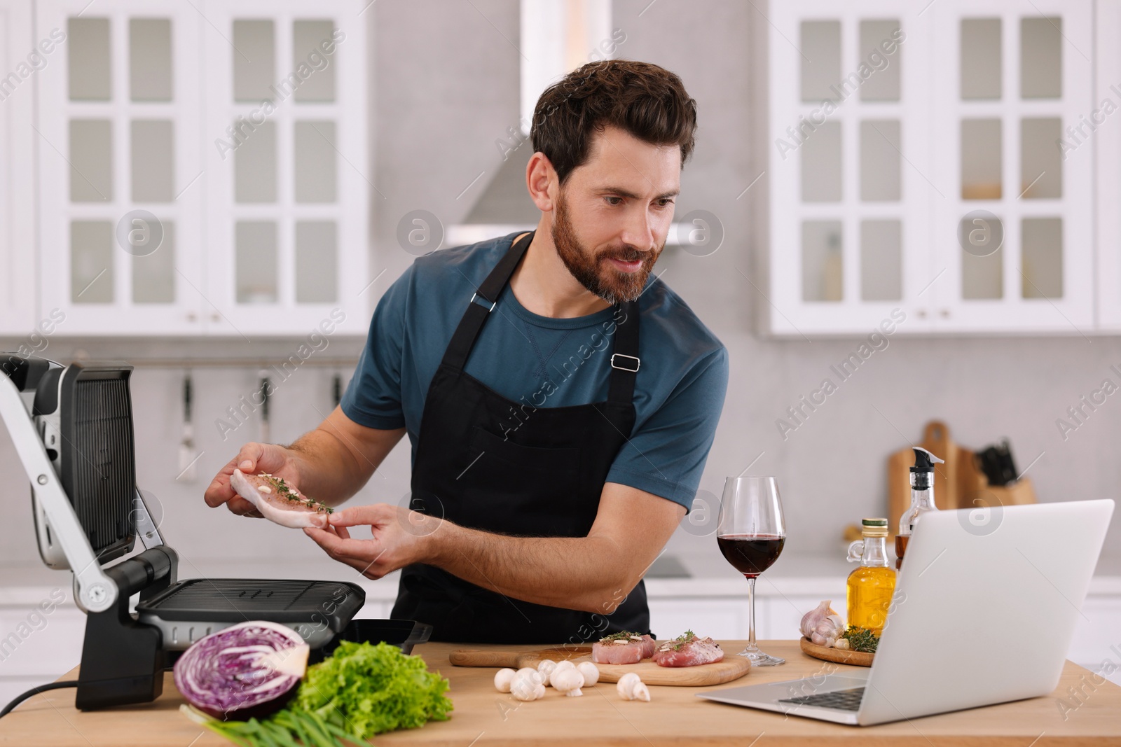 Photo of Man making dinner while watching online cooking course via laptop in kitchen