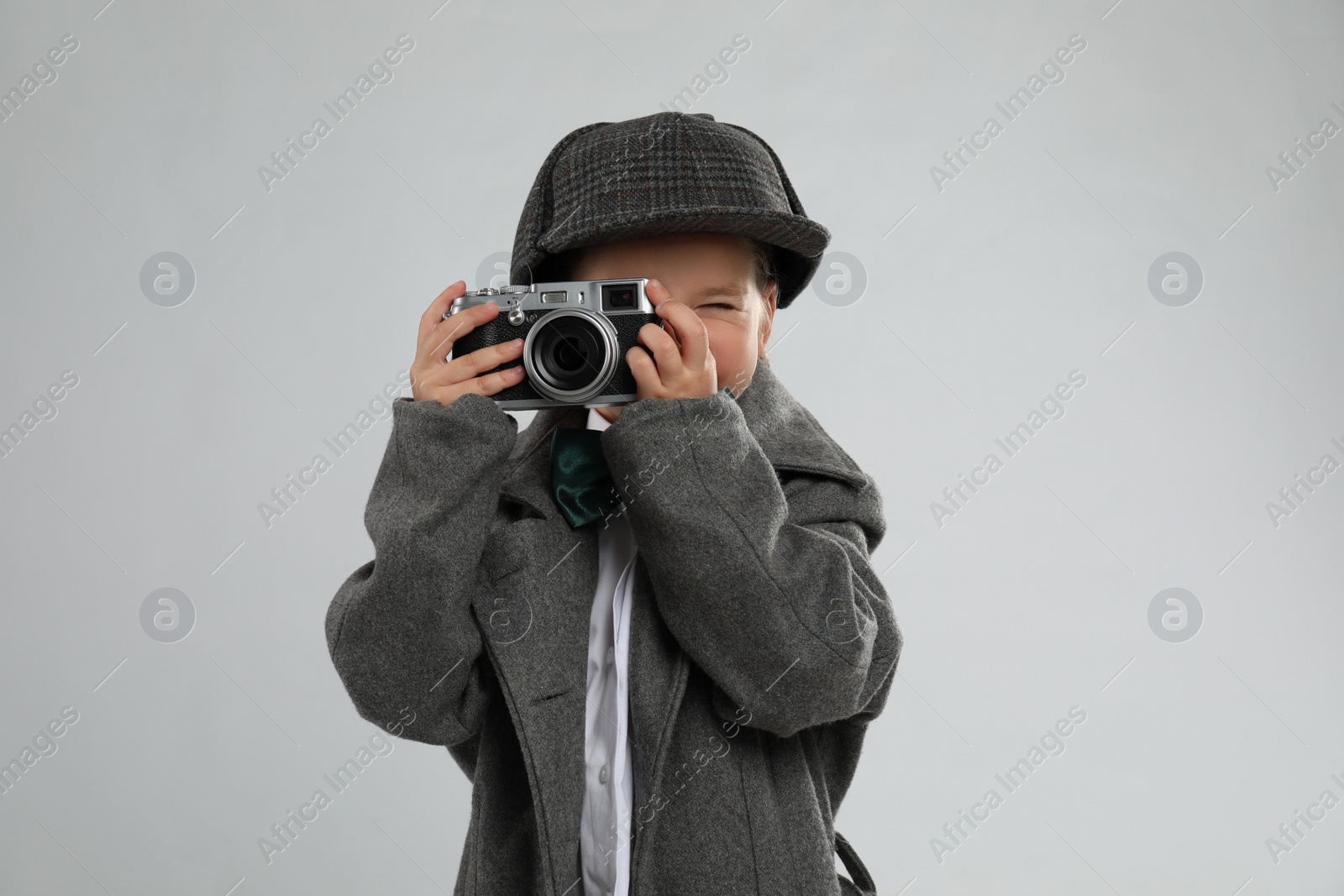 Photo of Cute little detective taking photo with vintage camera on grey background