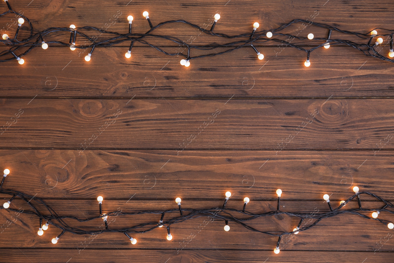 Photo of Glowing Christmas lights on wooden background, top view