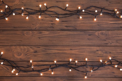 Photo of Glowing Christmas lights on wooden background, top view