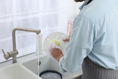 Man washing plate above sink in kitchen, closeup