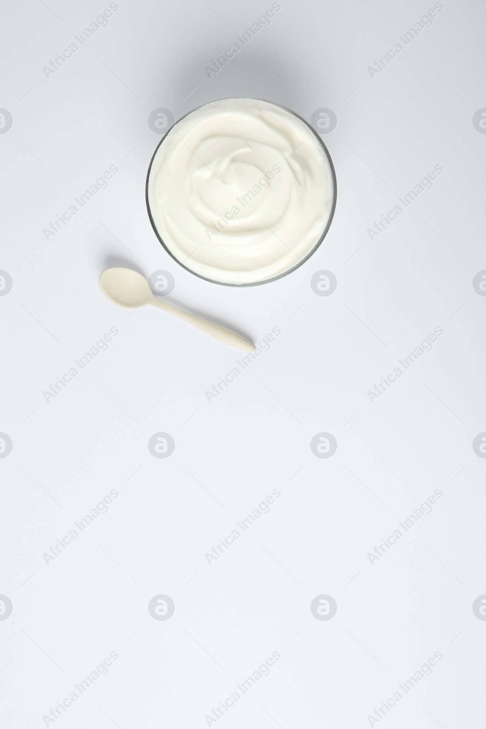 Photo of Glass bowl of sour cream and spoon on white background, top view