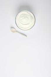 Photo of Glass bowl of sour cream and spoon on white background, top view