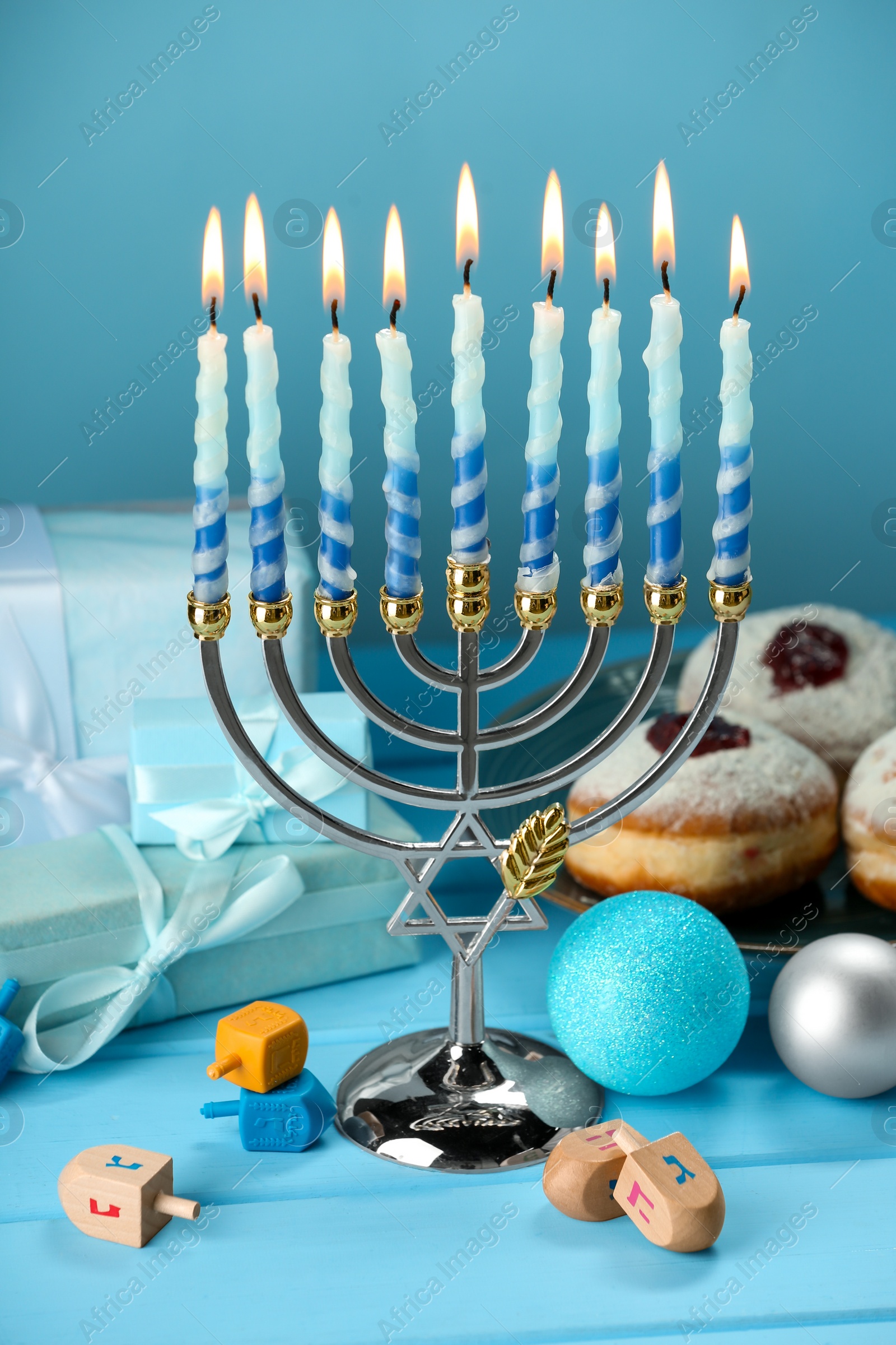Photo of Composition with Hanukkah menorah, dreidels, donuts and gift boxes on table against light blue background
