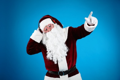 Photo of Santa Claus with headphones listening to Christmas music on blue background