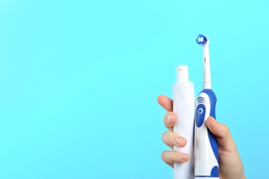 Photo of Woman holding electric toothbrush and paste on color background, space for text