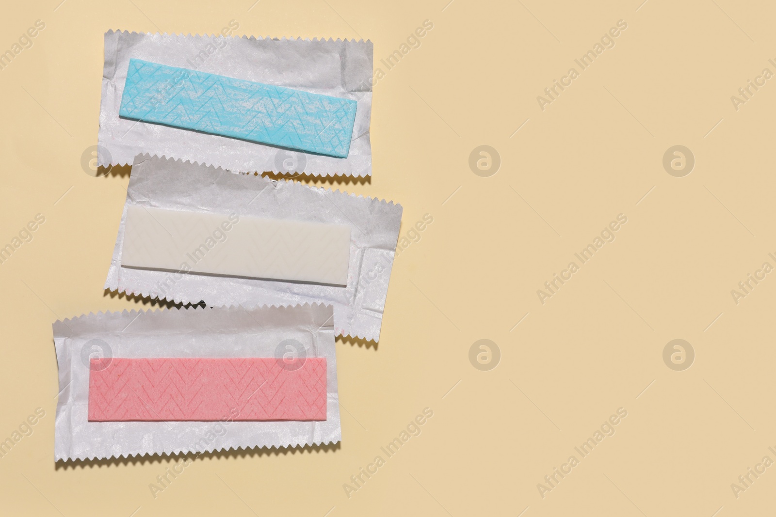 Photo of Unwrapped sticks of tasty chewing gum on beige background, flat lay. Space for text