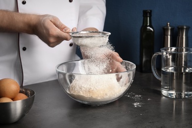 Man sprinkling dough for pastry with flour on table