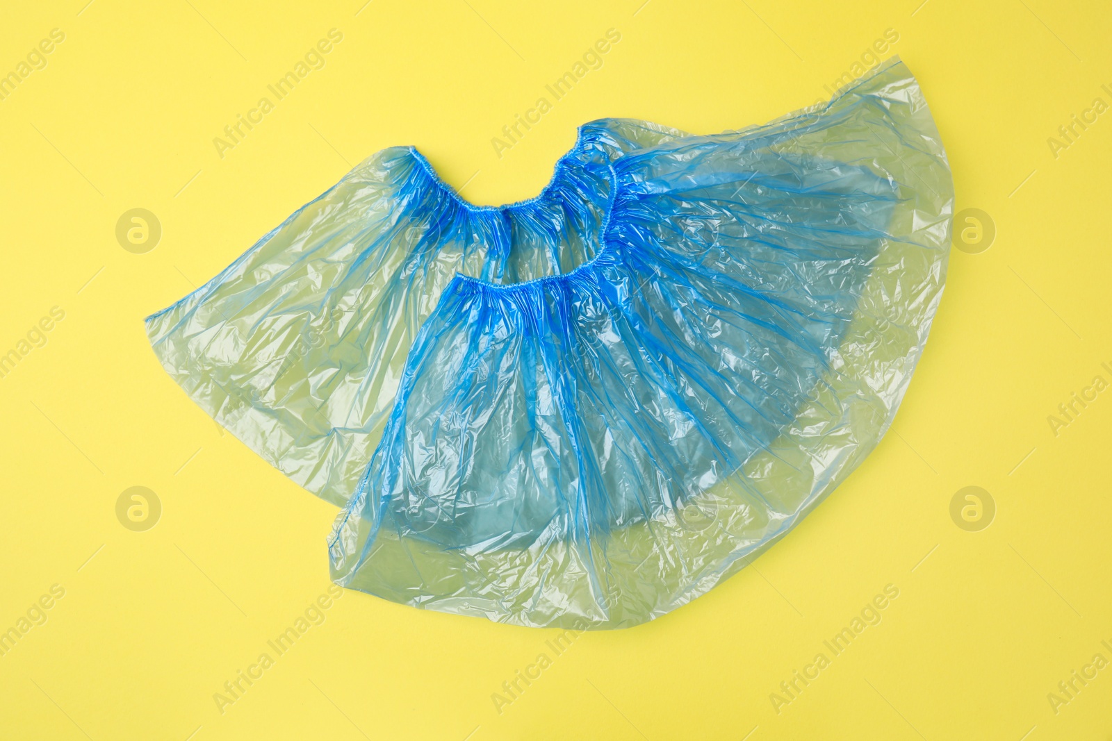 Photo of Pair of blue medical shoe covers on yellow background, top view