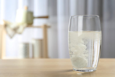 Photo of Glass of water with effervescent tablet on wooden table indoors, space for text