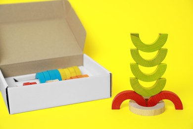 Photo of Colorful wooden pieces of playing set and box on yellow background. Educational toy for motor skills development