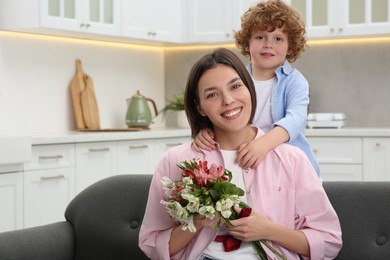 Photo of Little son congratulating his mom with Mother`s day at home, space for text. Woman holding bouquet of beautiful flowers