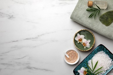 Flat lay composition with different spa products and flowers on white marble table. Space for text