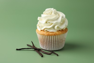 Tasty cupcake with cream and vanilla pods on green background