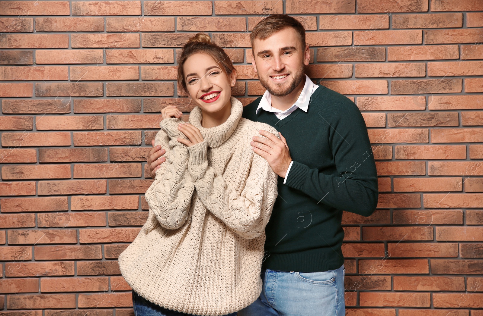 Photo of Young couple in warm sweaters near brick wall