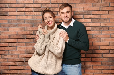 Young couple in warm sweaters near brick wall