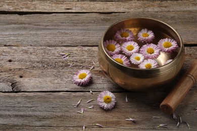 Photo of Tibetan singing bowl with water, chrysanthemum flowers and mallet on wooden table, space for text