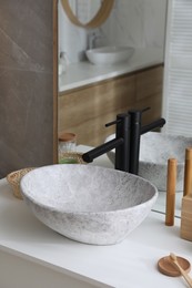 Stone vessel sink with faucet and toiletries on white countertop in bathroom