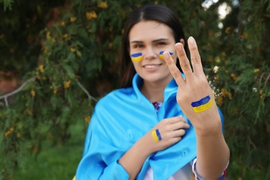 Young woman showing Ukrainian trident gesture outdoors, focus on hand. Space for text