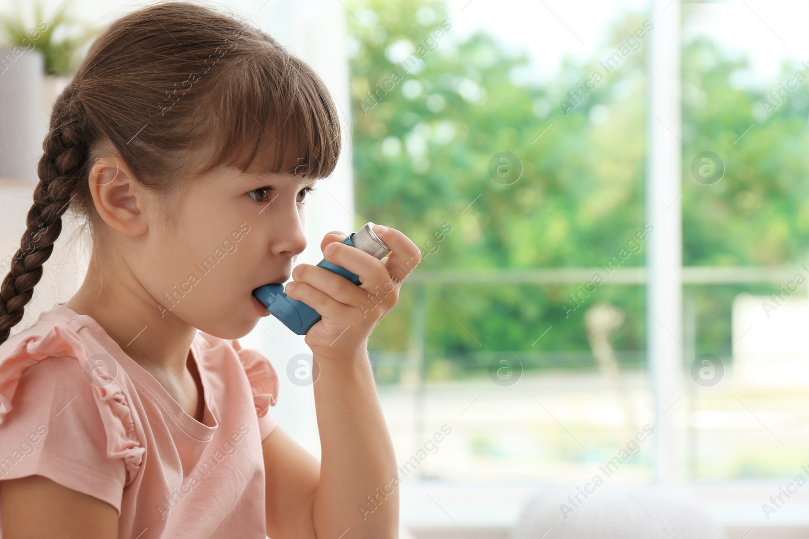 Photo of Little girl using asthma inhaler on blurred background