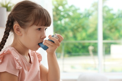 Little girl using asthma inhaler on blurred background